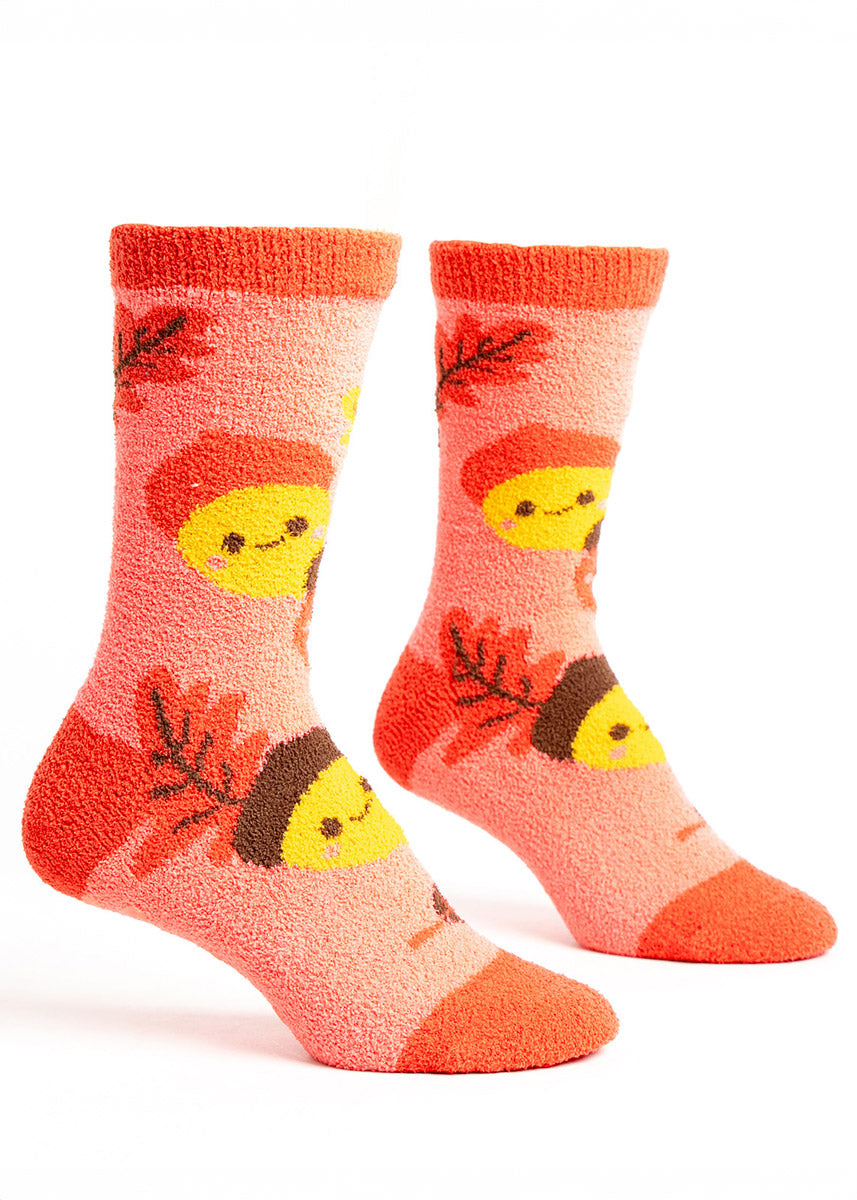 Pink fuzzy slipper socks for women with a pattern of cartoon acorns with smiley faces and autumn leaves in shades of orange, yellow, and brown.