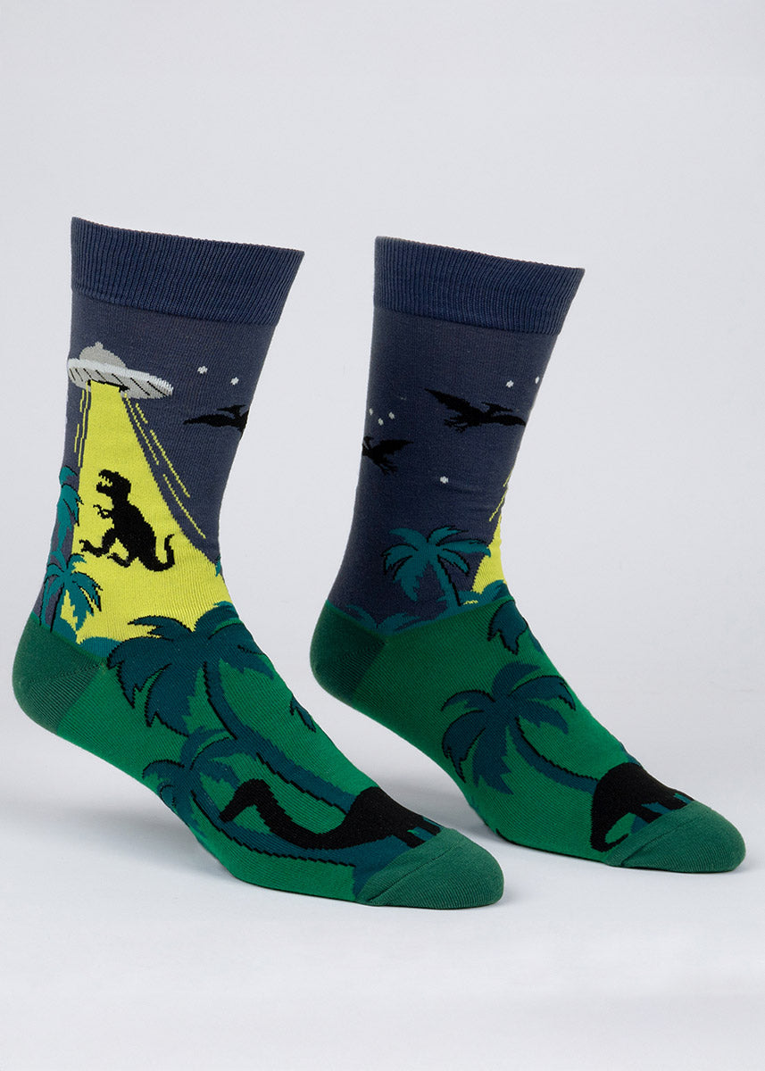 Blue and green novelty crew socks for men featuring a lush prehistoric scene of various dinosaurs, including a T-Rex getting beamed up by a UFO.