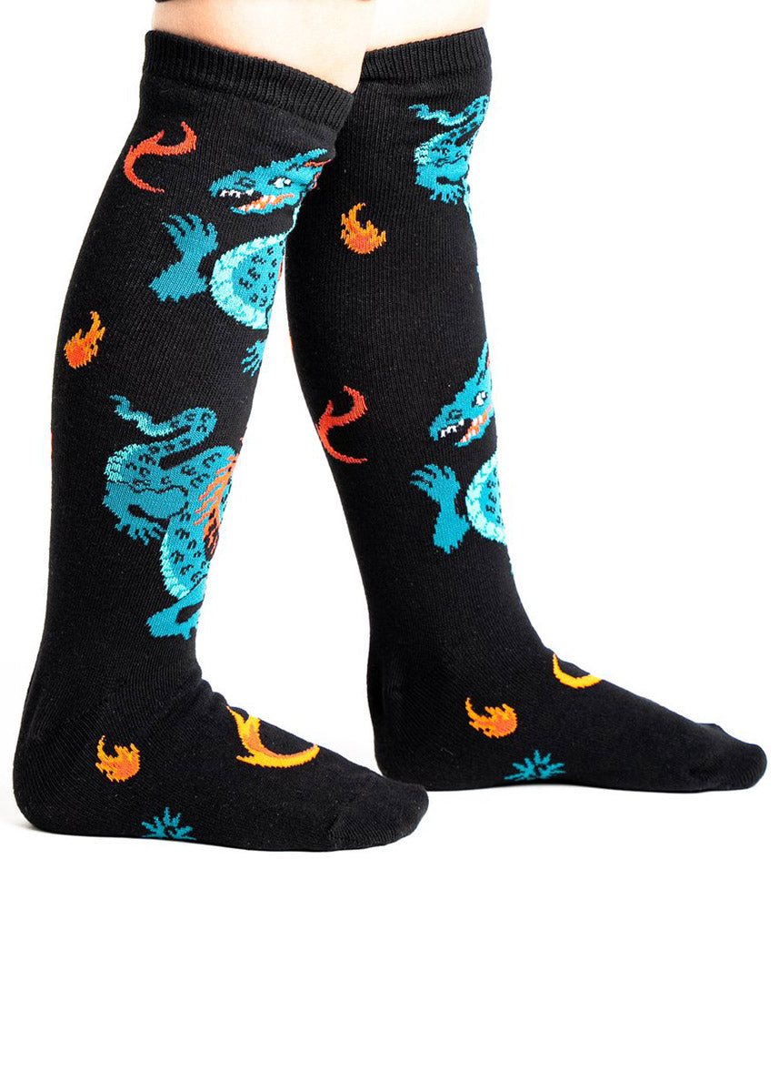 Black knee socks for kids with green dragons wrapping around the leg along with bits of fire. 