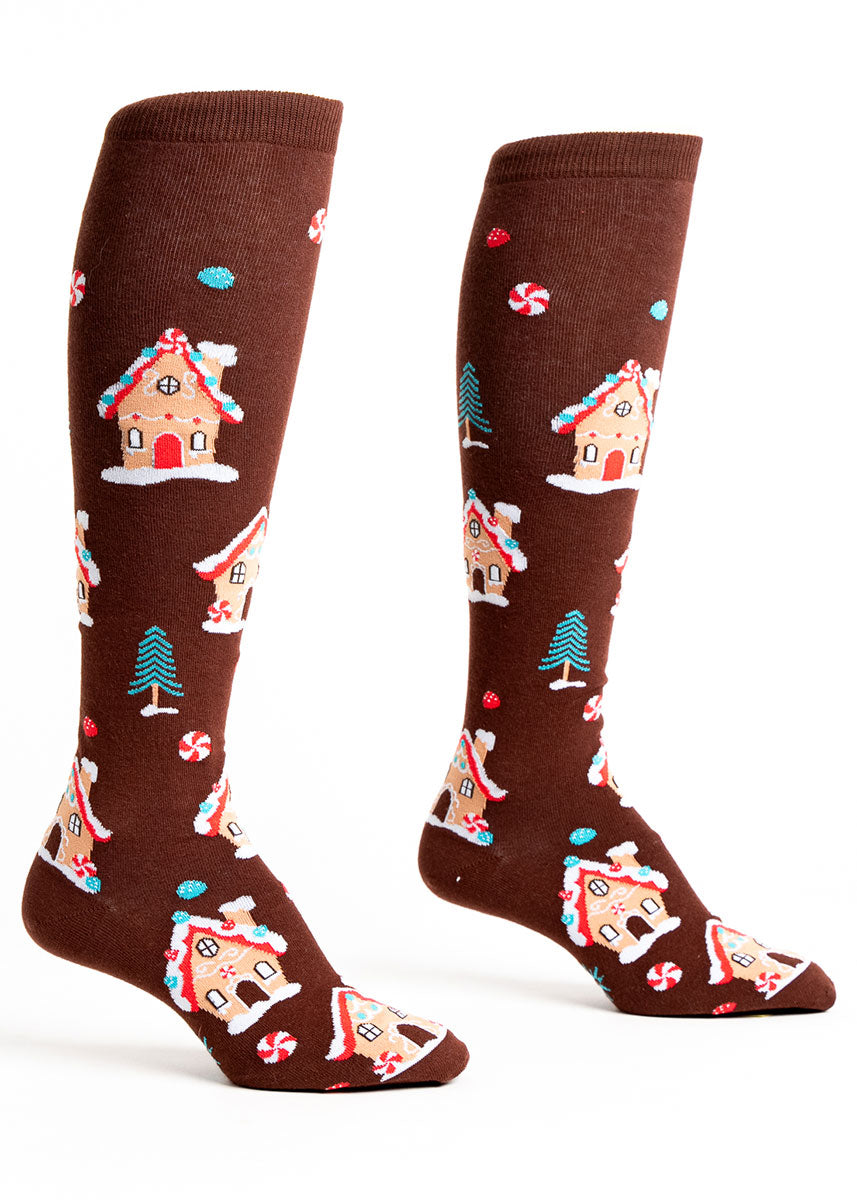 Brown knee socks for women with an allover pattern of gingerbread houses  and bits of candy such as peppermint and gumdrops.