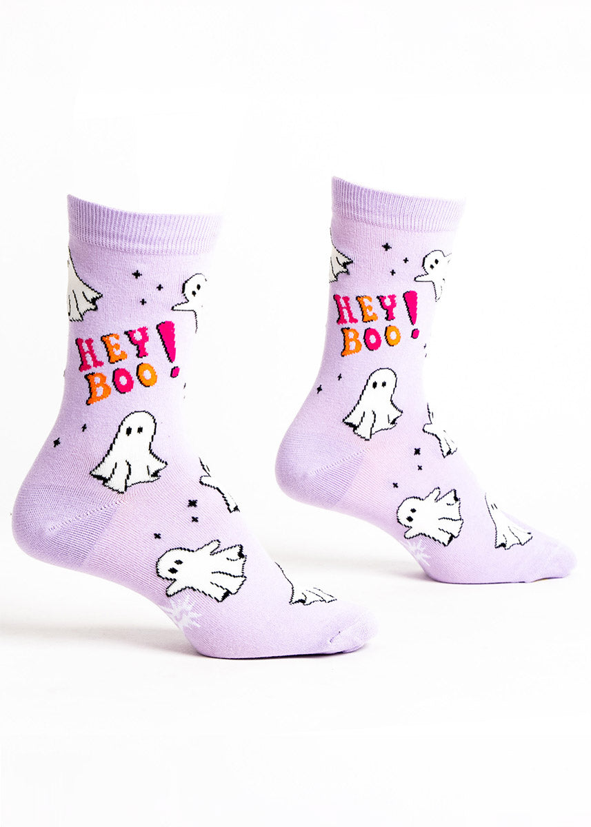 Light purple crew socks for women with a pattern of white ghosts that glow in the dark and the phrase &quot;Hey Boo!&quot; in pink and orange lettering.