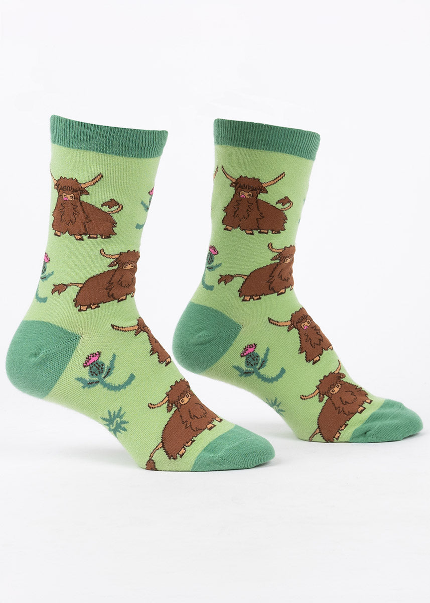 Green crew socks for women with a pattern of furry brown highland cows and thistles. 