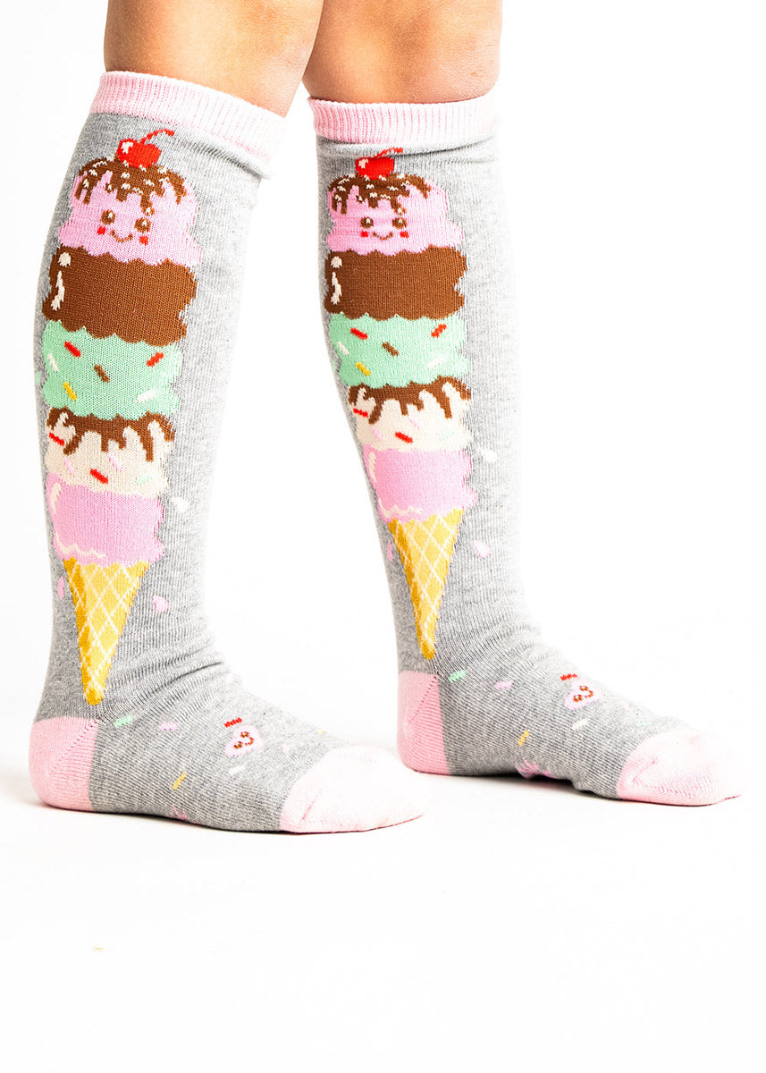 Gray knee socks for kids featuring an ice cream cone with many colorful scoops stacked along the leg with the top scoop having a smiley face and a cherry on top.