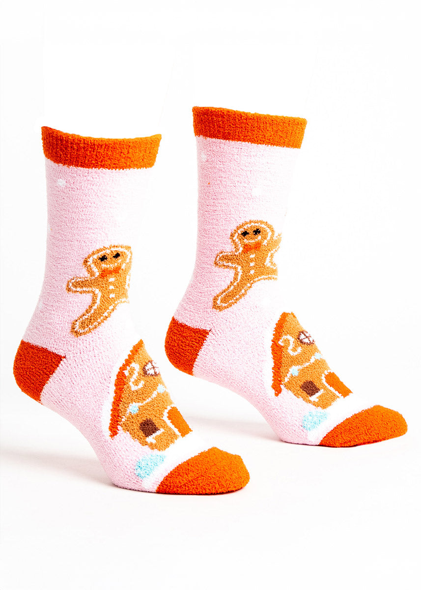 Pink fuzzy slipper socks for women with an orange cuff, heel and toe and a gingerbread man and gingerbread house design. 