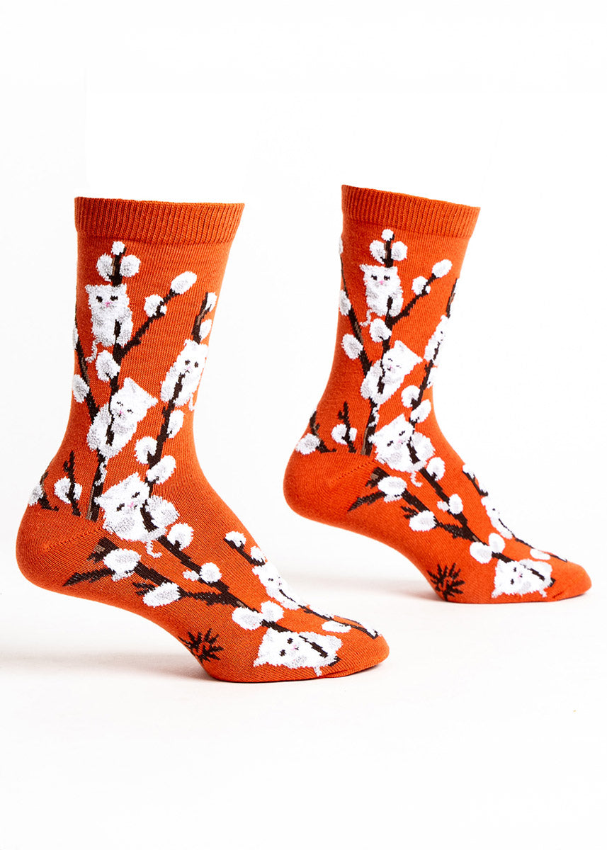 Orange crew socks for women with a design of white 3D fuzzy pussy willow stalks where some of the blooms are white cats. 