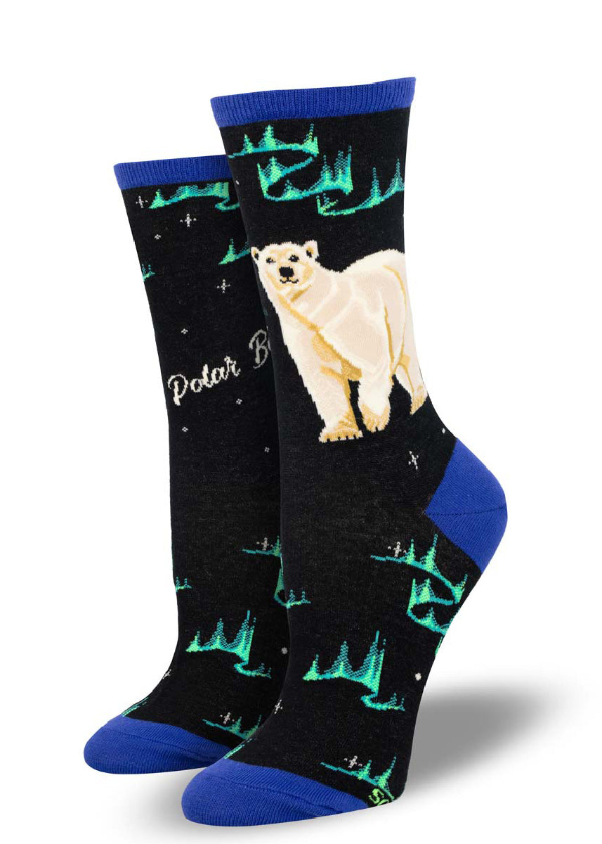 Black crew socks for women that feature a white polar bear against a backdrop of teal northern lights and stars.