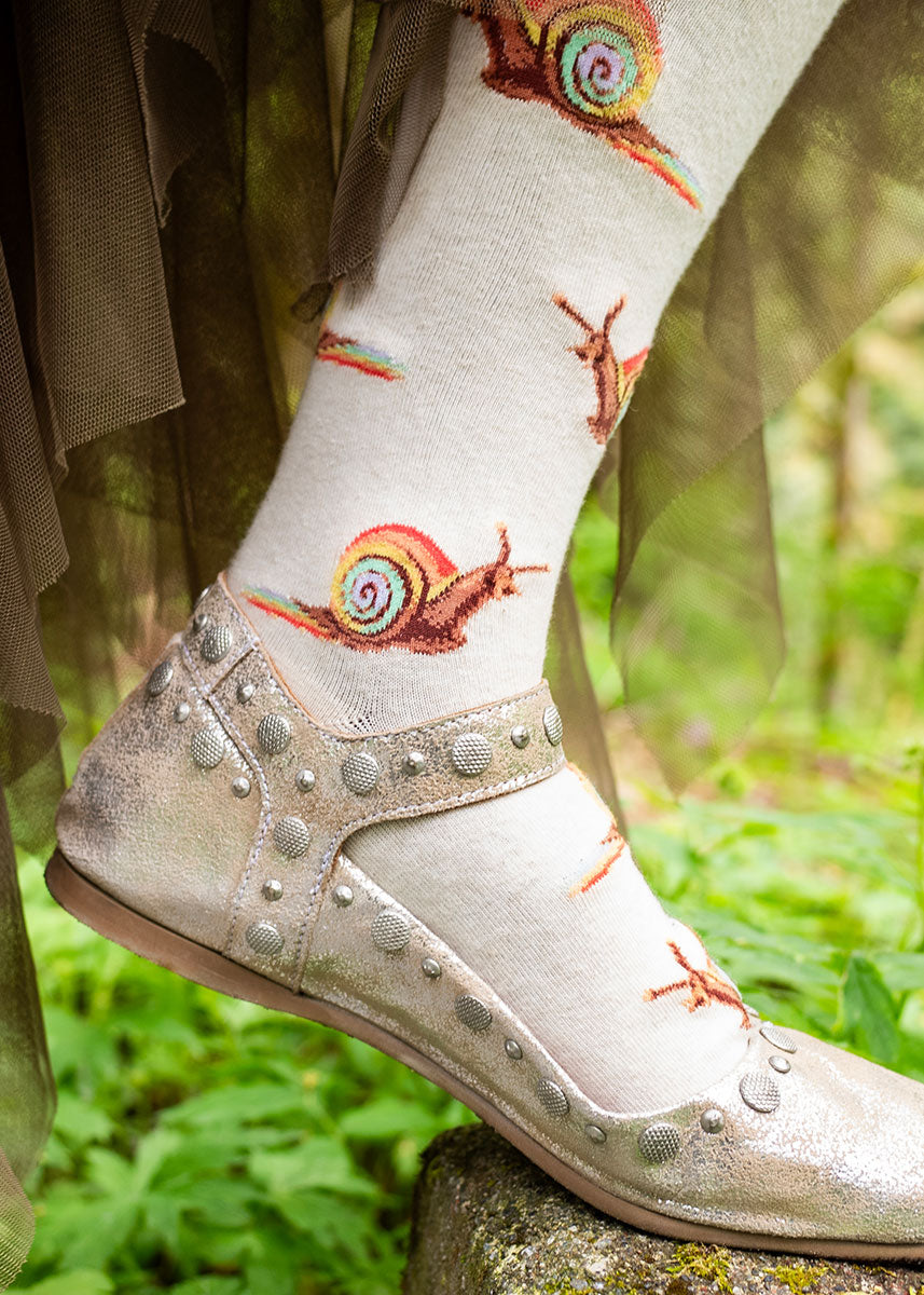 Cream knee socks for women with an allover pattern of brown snails with pastel rainbow shells leaving a rainbow slime trail behind them.