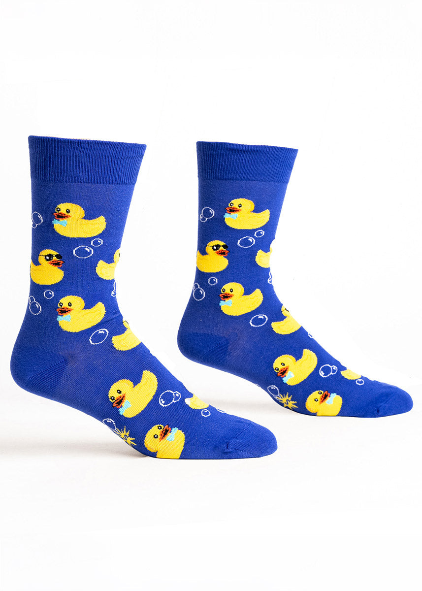 Blue novelty crew socks for men with a pattern of bubbles and yellow rubber ducks wearing bow ties and sunglasses. 