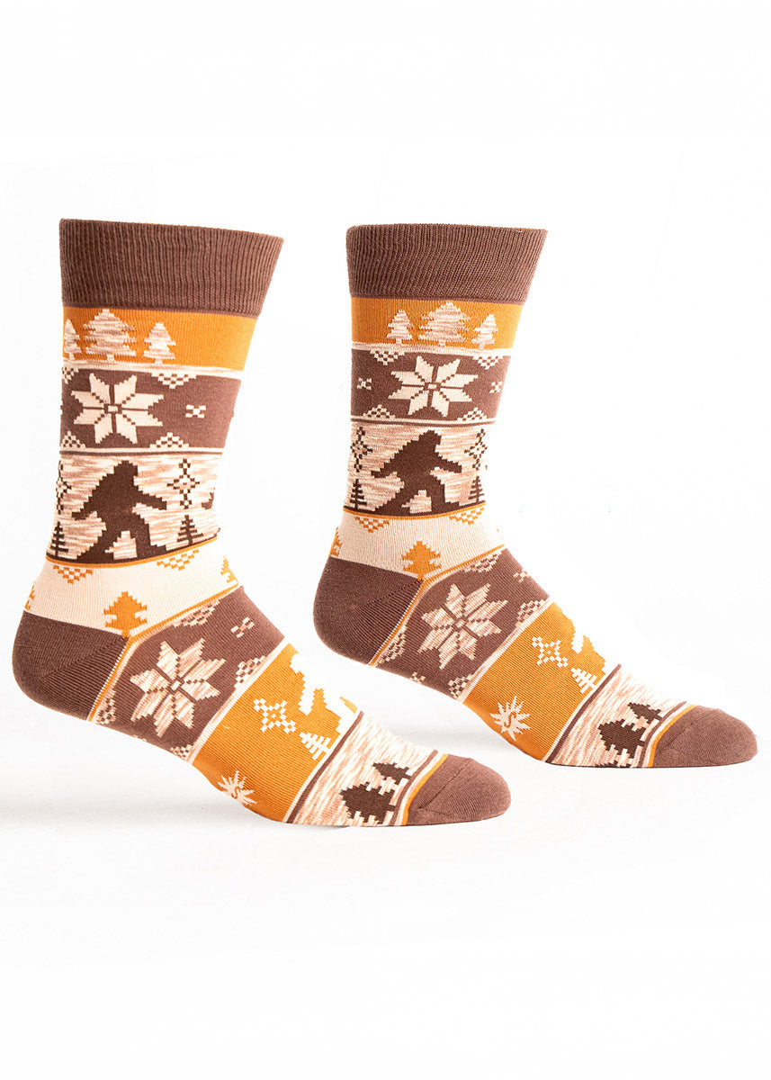 Brown crew socks for men with an ugly sweater pattern in shades of brown that features a Sasquatch and pine trees. 