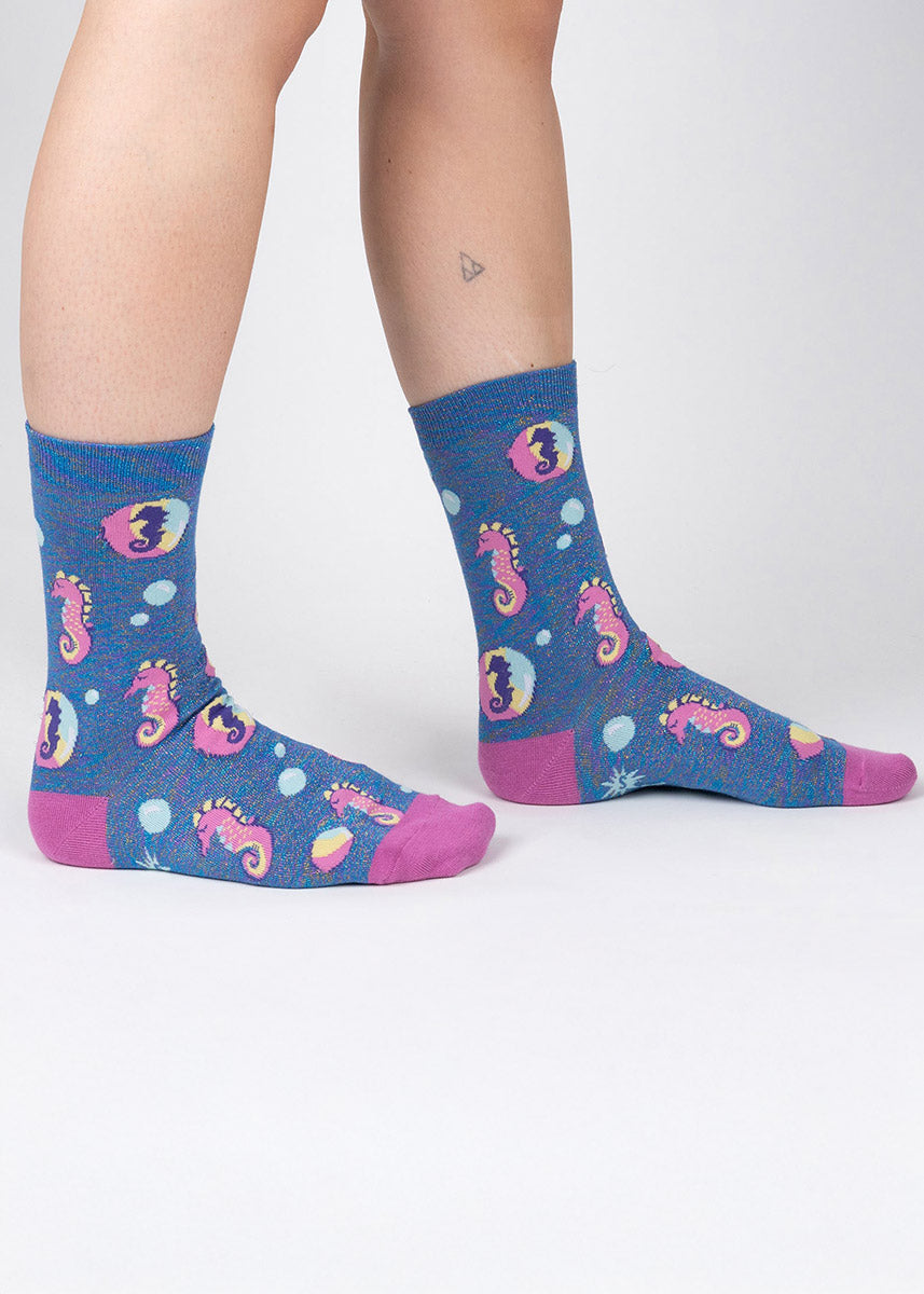 Blue novelty crew socks with shimmery rainbow thread for women feature an allover pattern of pink seahorses and bubbles.