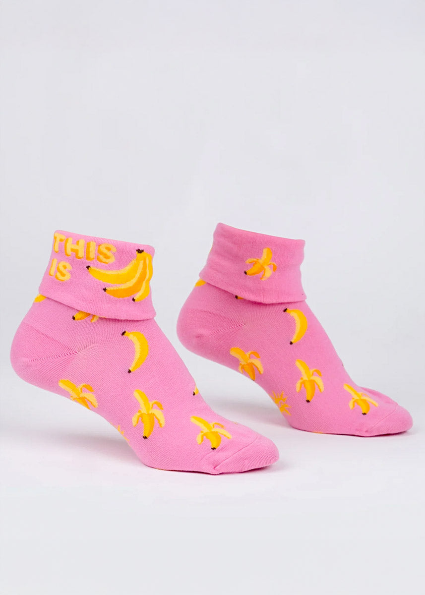 Pink turn-cuff ankle socks with an allover pattern of yellow bananas that say &quot;This Is&quot; followed by a bunch of bananas on the cuff.