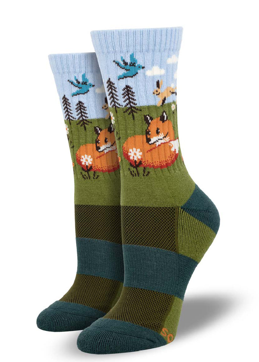 Blue and green wool hiking socks for women featuring woodland creatures such as a fox, hare, and blue bird in a floral meadow scene.