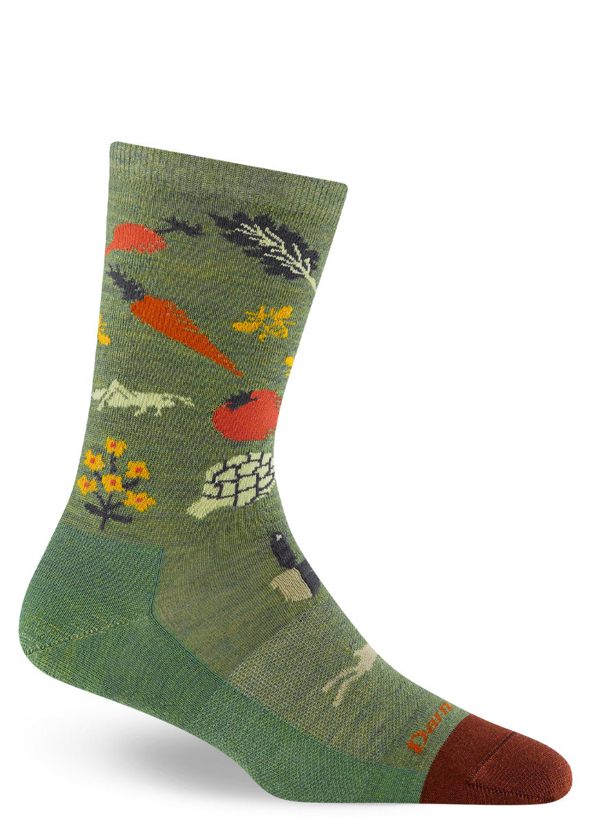 Wool socks for women feature a garden design of veggies, flowers, bees, and tools on a green background.